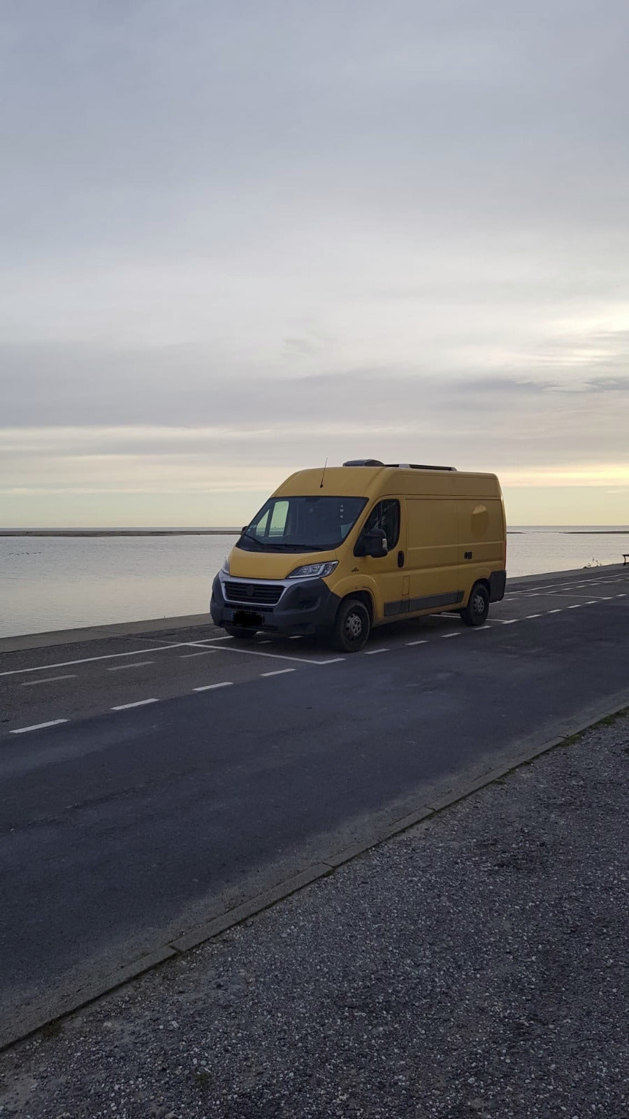 Van au bord de la mer, garé sur une place de parking.